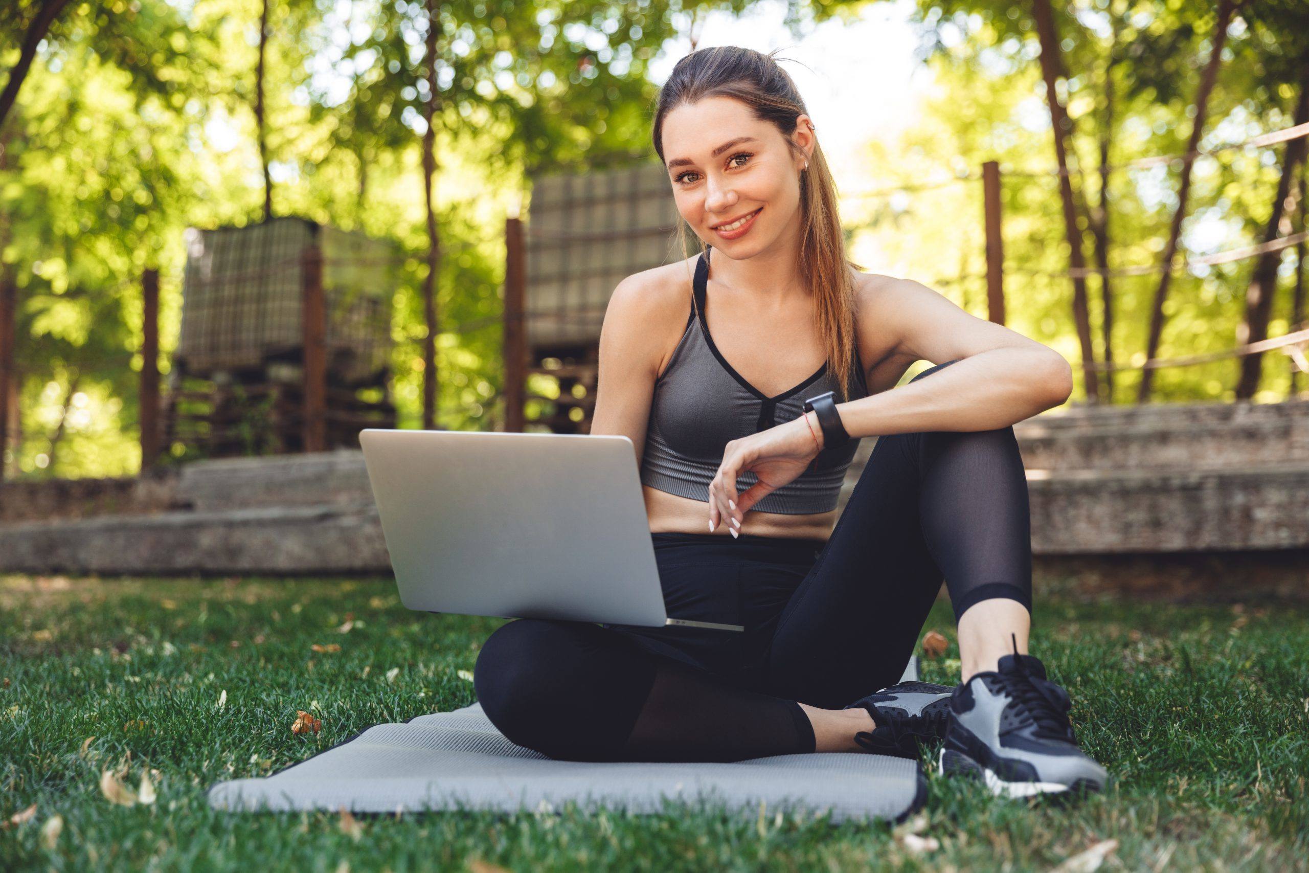 Portrait of a smiling young fitness girl using laptop